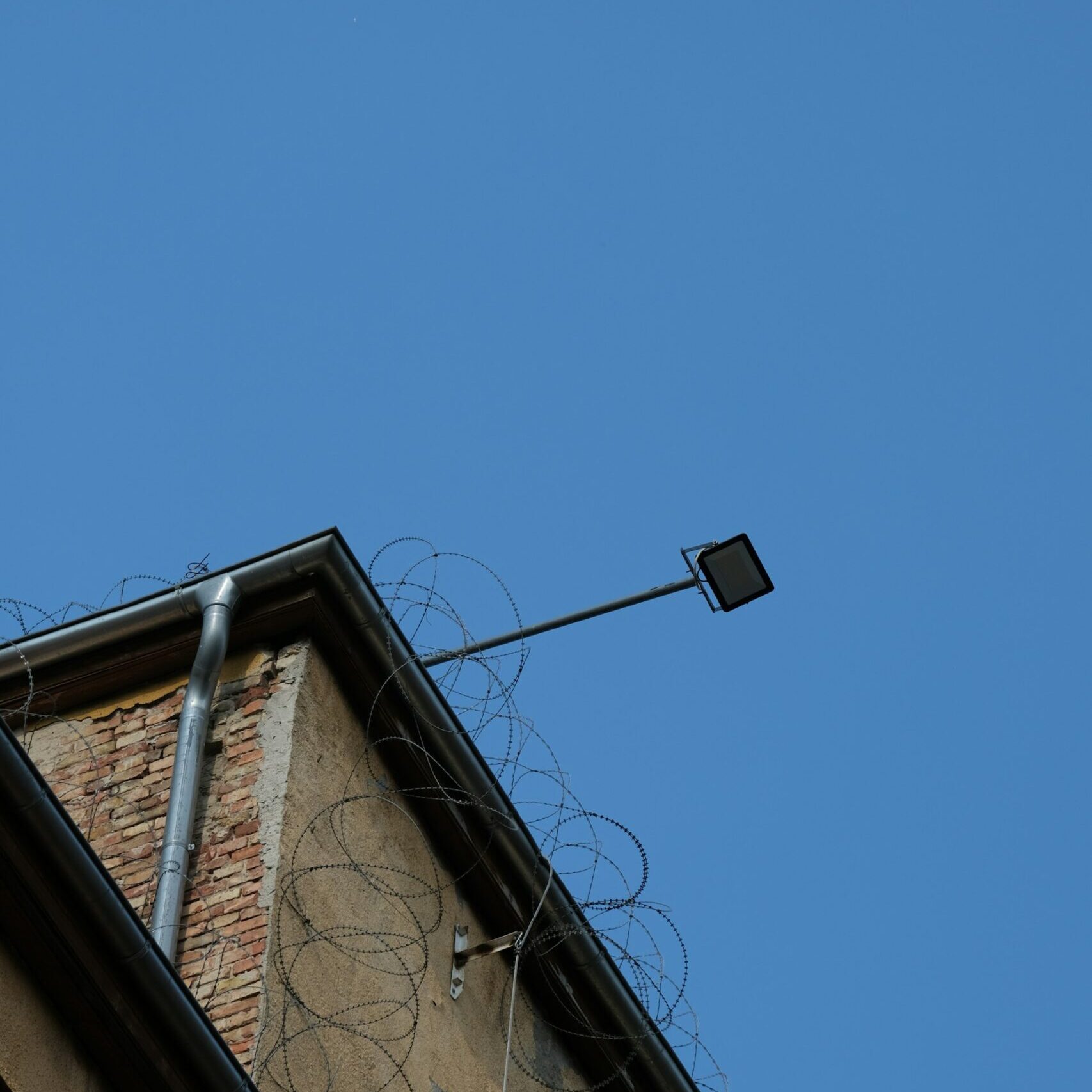 Barbed wire on the roof of a building against a clear blue sky.